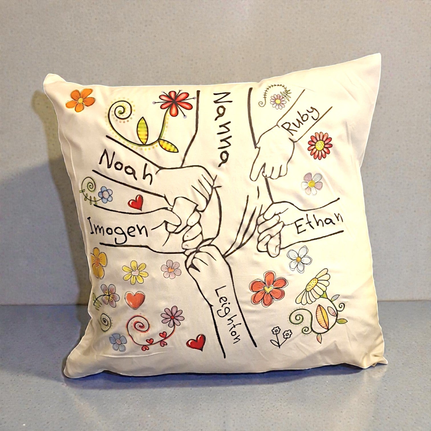 Decorative pillow with hand-drawn design of hands holding hands and names, on a plain background.