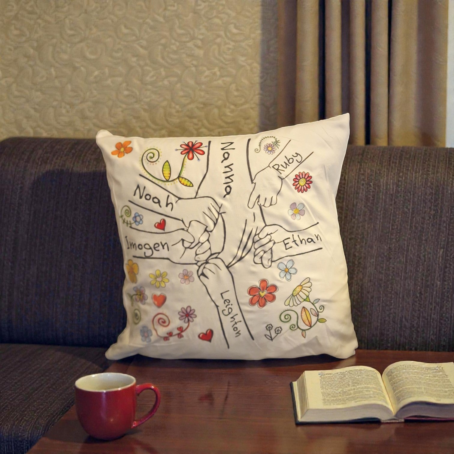Decorative pillow with embroidered names on a couch next to a mug and book