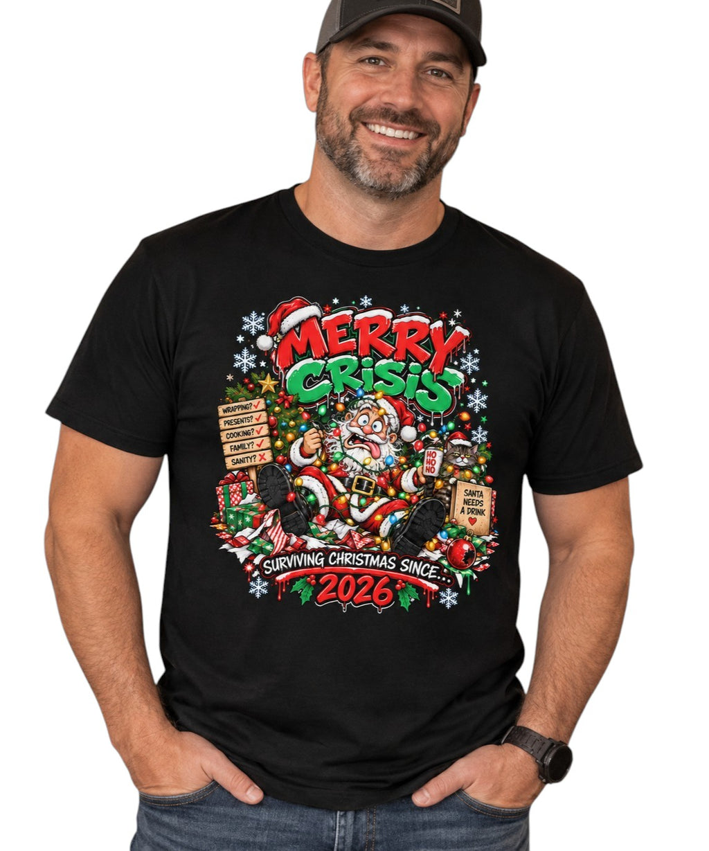 A man wearing a black graphic t-shirt with a colorful 'Merry Crisis' Christmas-themed print, standing against a plain white background.