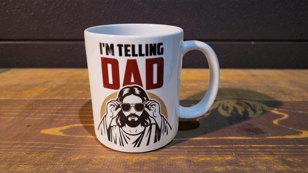 White mug with a graphic of a man and text 'I'm Telling Dad' on a wooden surface.