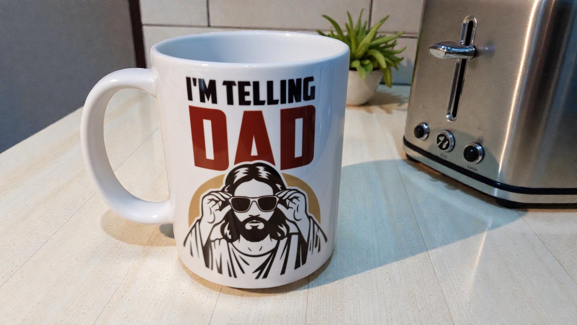 Mug with 'I'm Telling Dad' text and graphic on a kitchen counter with a toaster.