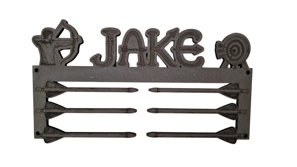 A cast iron archery wall sign featuring the name 'JAKE' in raised letters, flanked by a bow silhouette on the left and a target silhouette on the right. Below the name, the sign holds five arrows on a plain white background.