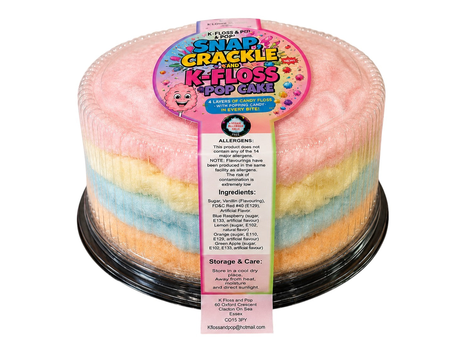 A round, multi-colored cotton candy cake in a clear plastic container with a black base, featuring a colorful paper label that reads 'Flavors by Pop! Snap Crackle K-Floss Pop Cake'. The cotton candy layers are pastel pink, yellow, and light blue.