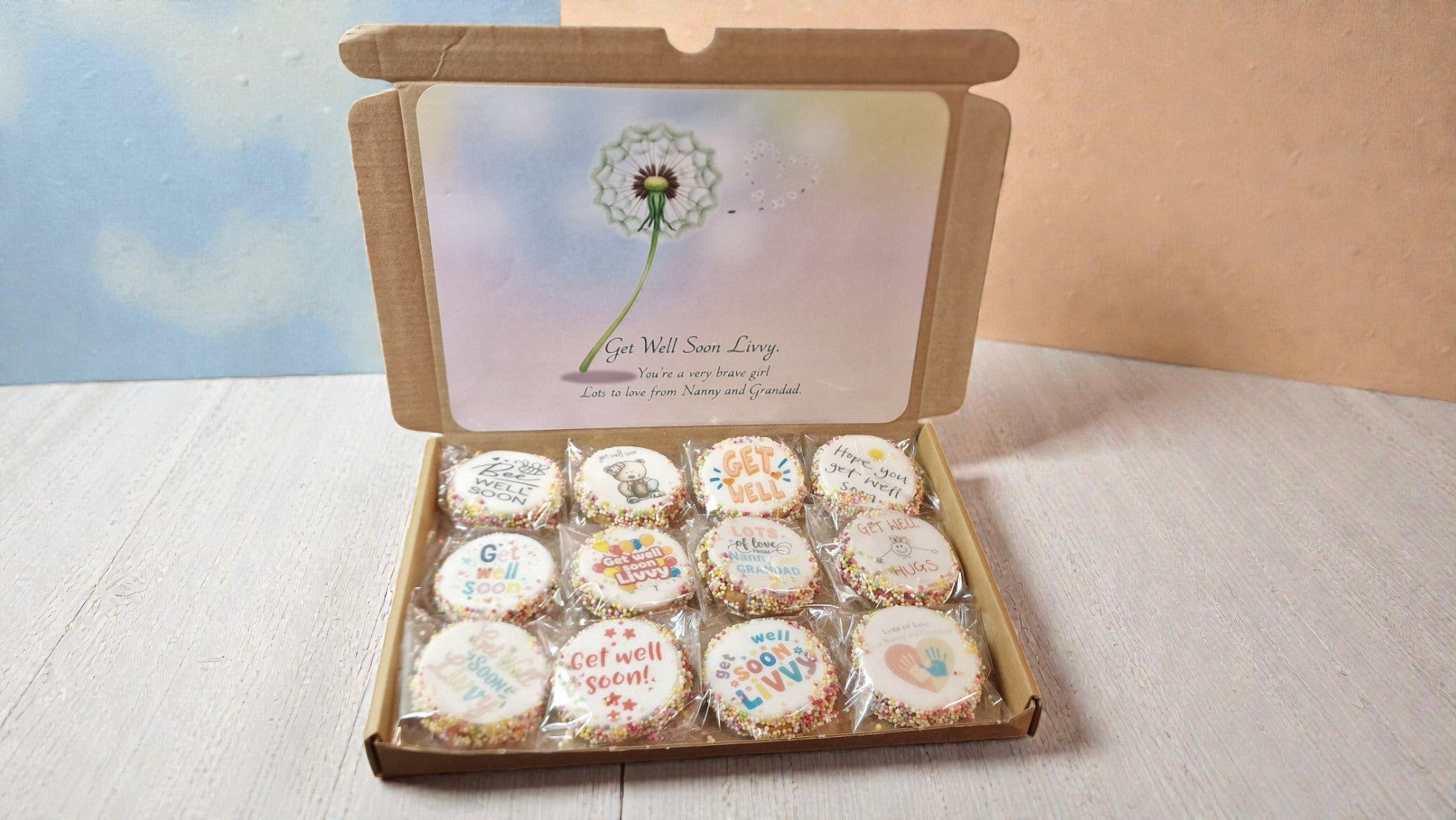 Box of small round cookies with personalized messages on a light surface.