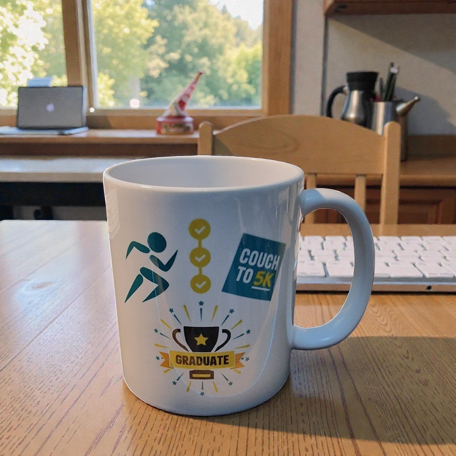 Couch to 5K Graduate mug on a desk with a laptop and window in the background