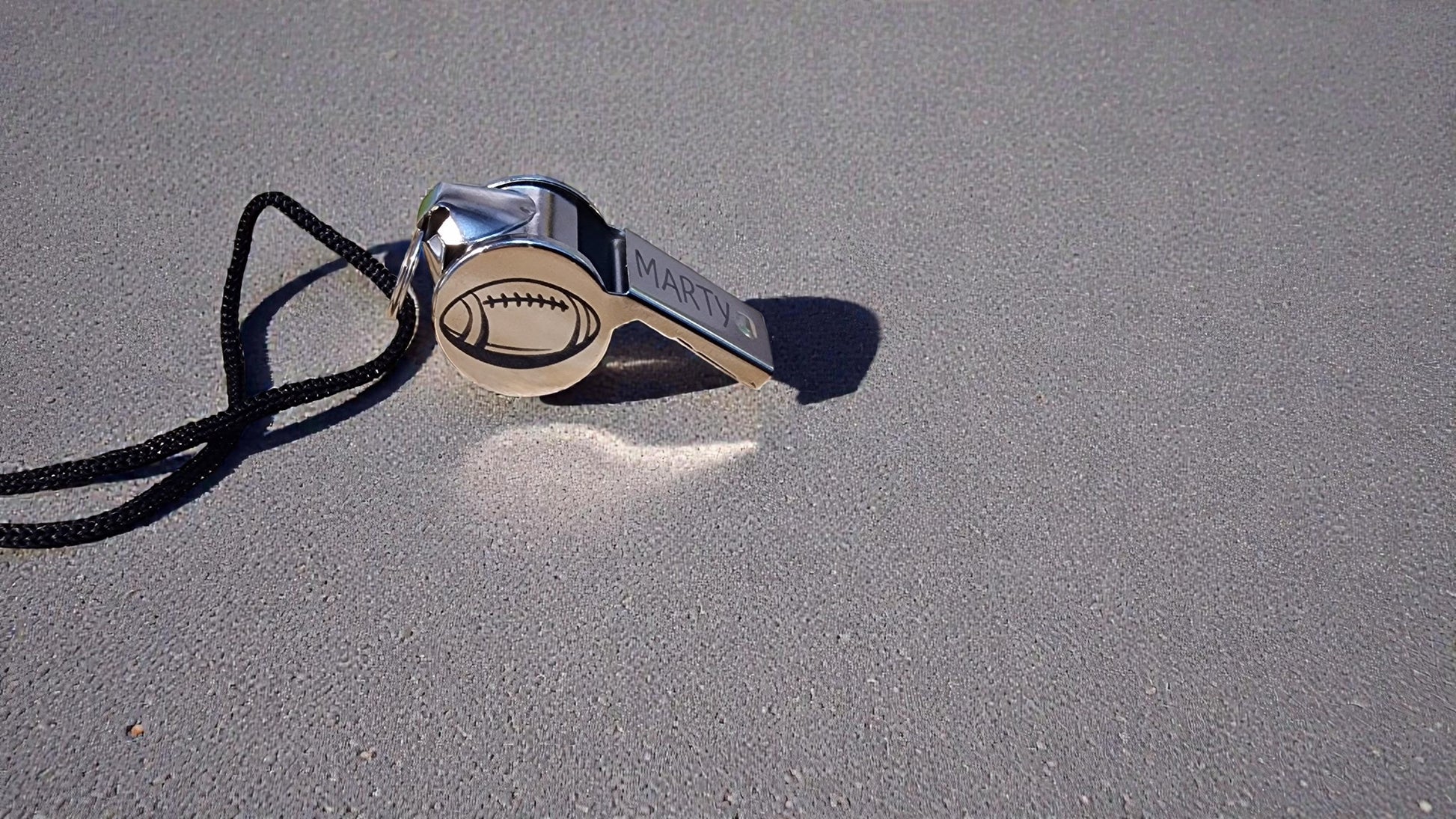 Metallic whistle with a football design on a gray surface