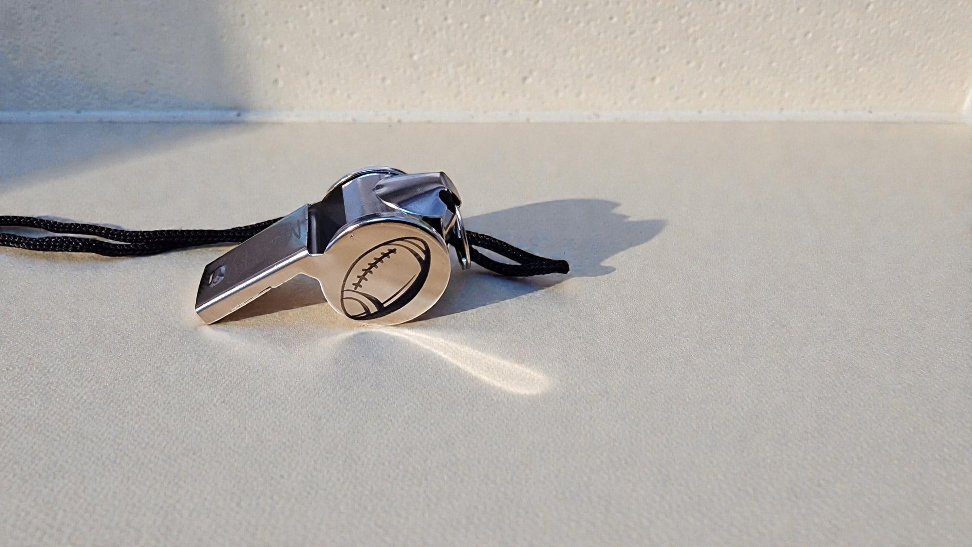 Silver whistle with a black lanyard on a white surface