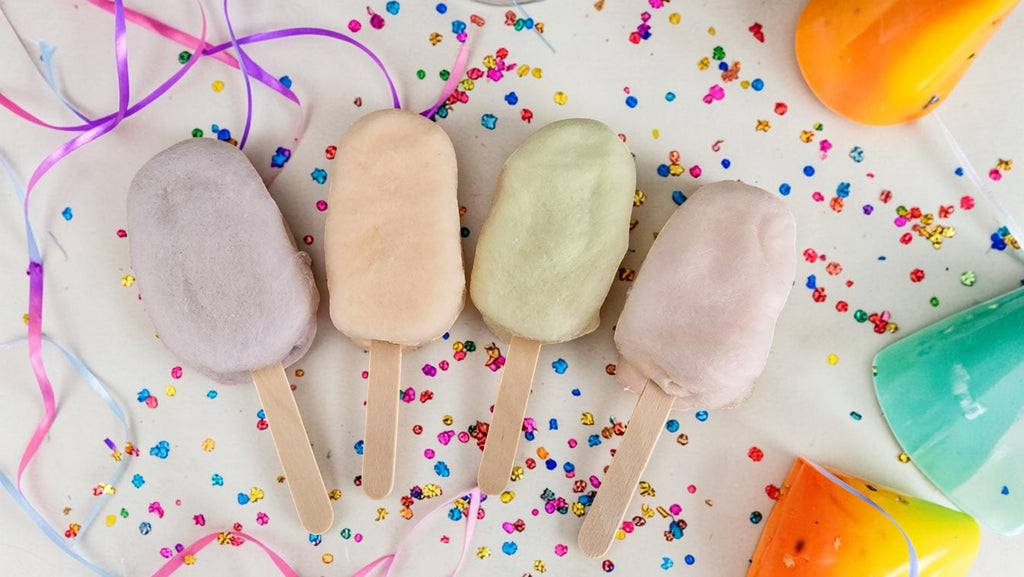 Four popsicles on a surface with colorful confetti and ribbons.