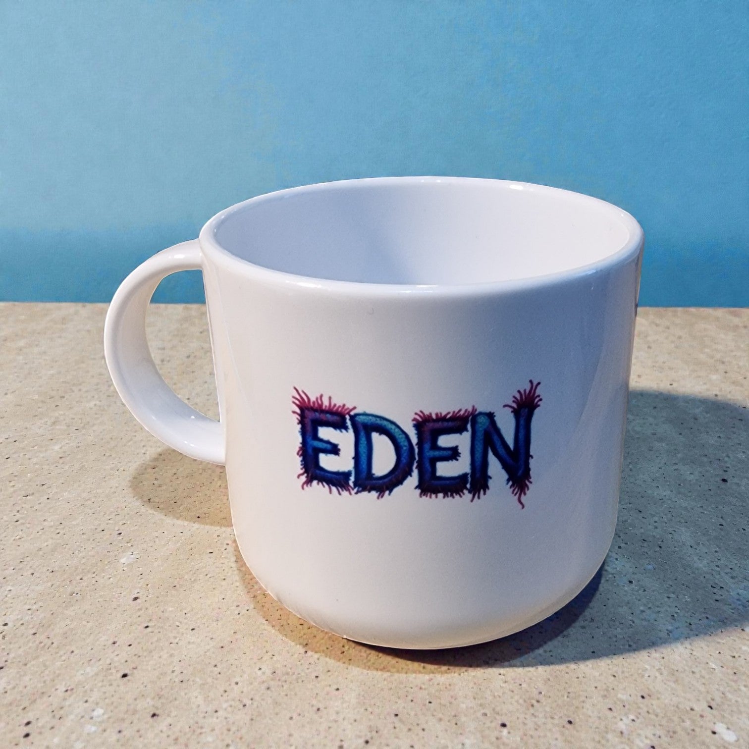 White mug with 'EDEN' printed on it against a blue sky background