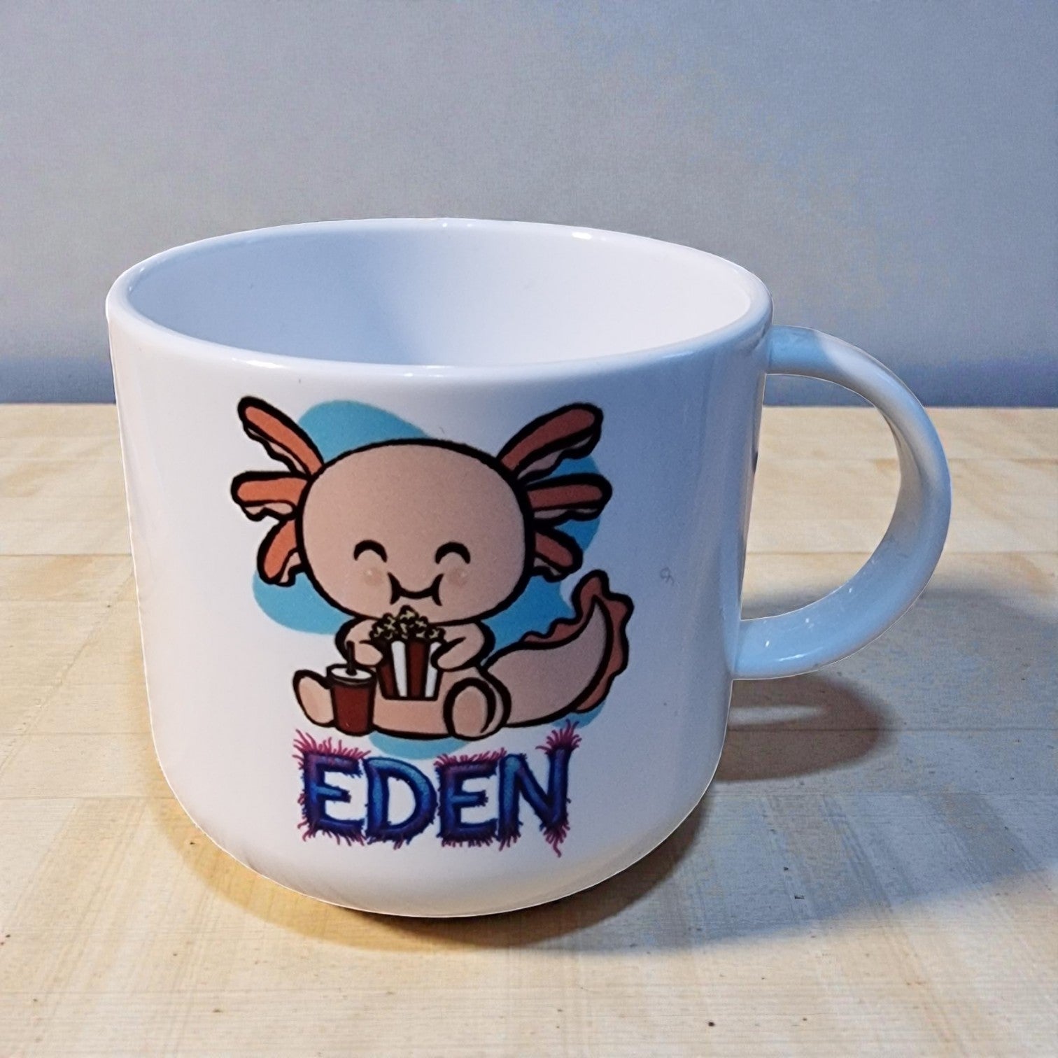 White mug with cartoon character and 'EDEN' text on a wooden surface