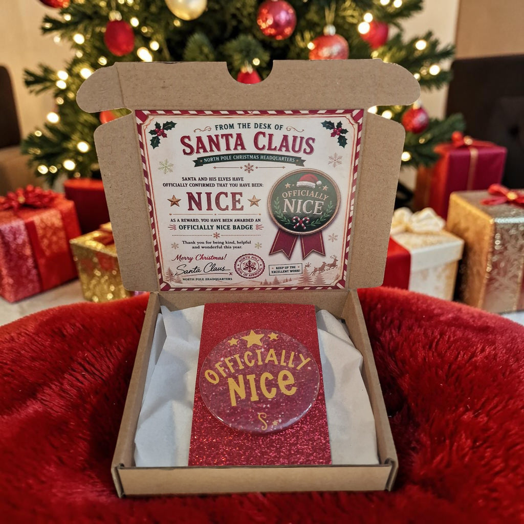 Box with 'Officially Nice' badge and certificate from Santa Claus against a Christmas tree and gift background