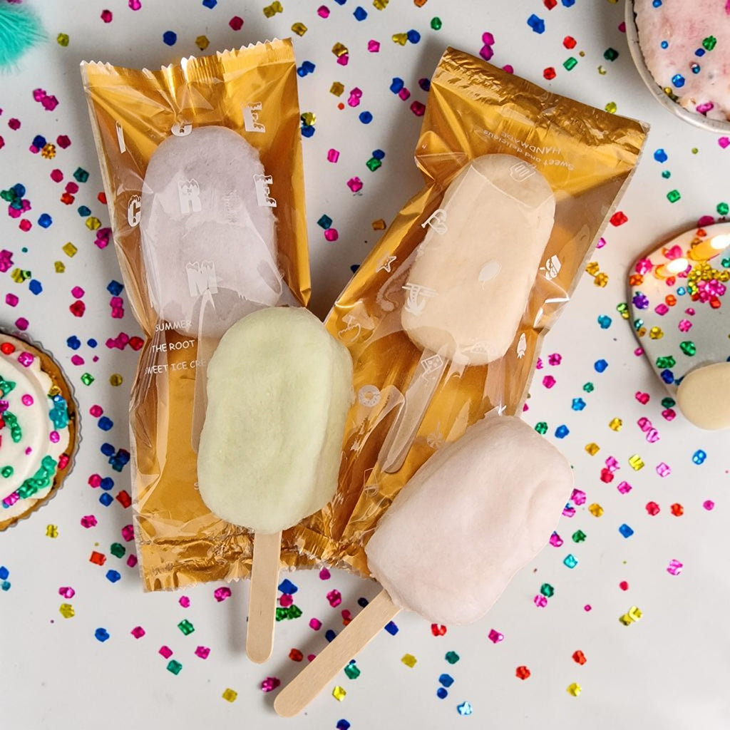 Two popsicles in gold packaging on a colorful confetti background