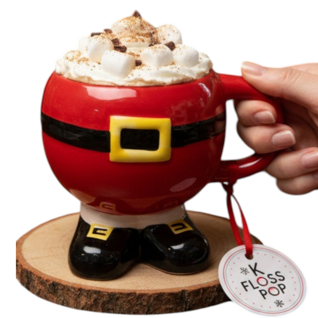 Red Santa mug with hot chocolate and marshmallows, held by a hand, on a wooden coaster with 'K Floss Pop' tag.