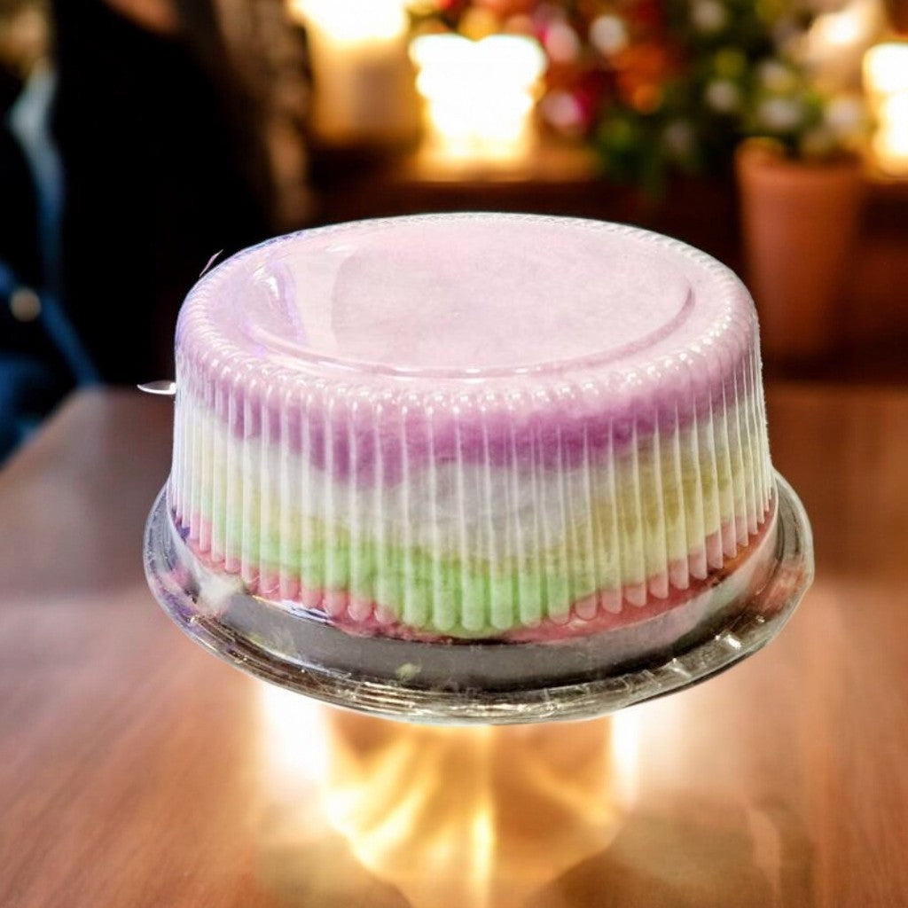 Small round cake with pink and green layers on a clear cake stand.