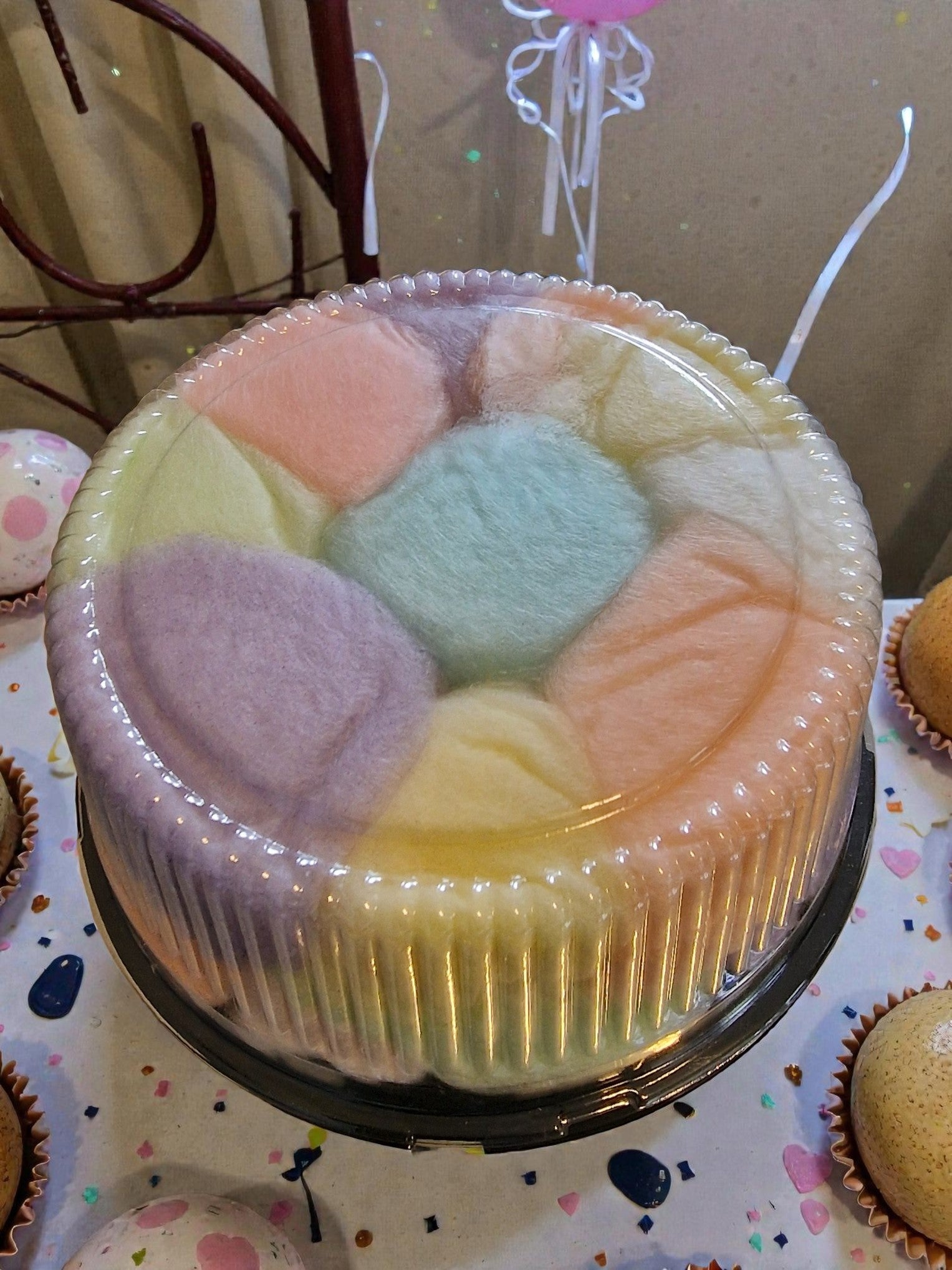 Pastel-colored yarn balls in a clear container on a table with cupcakes.