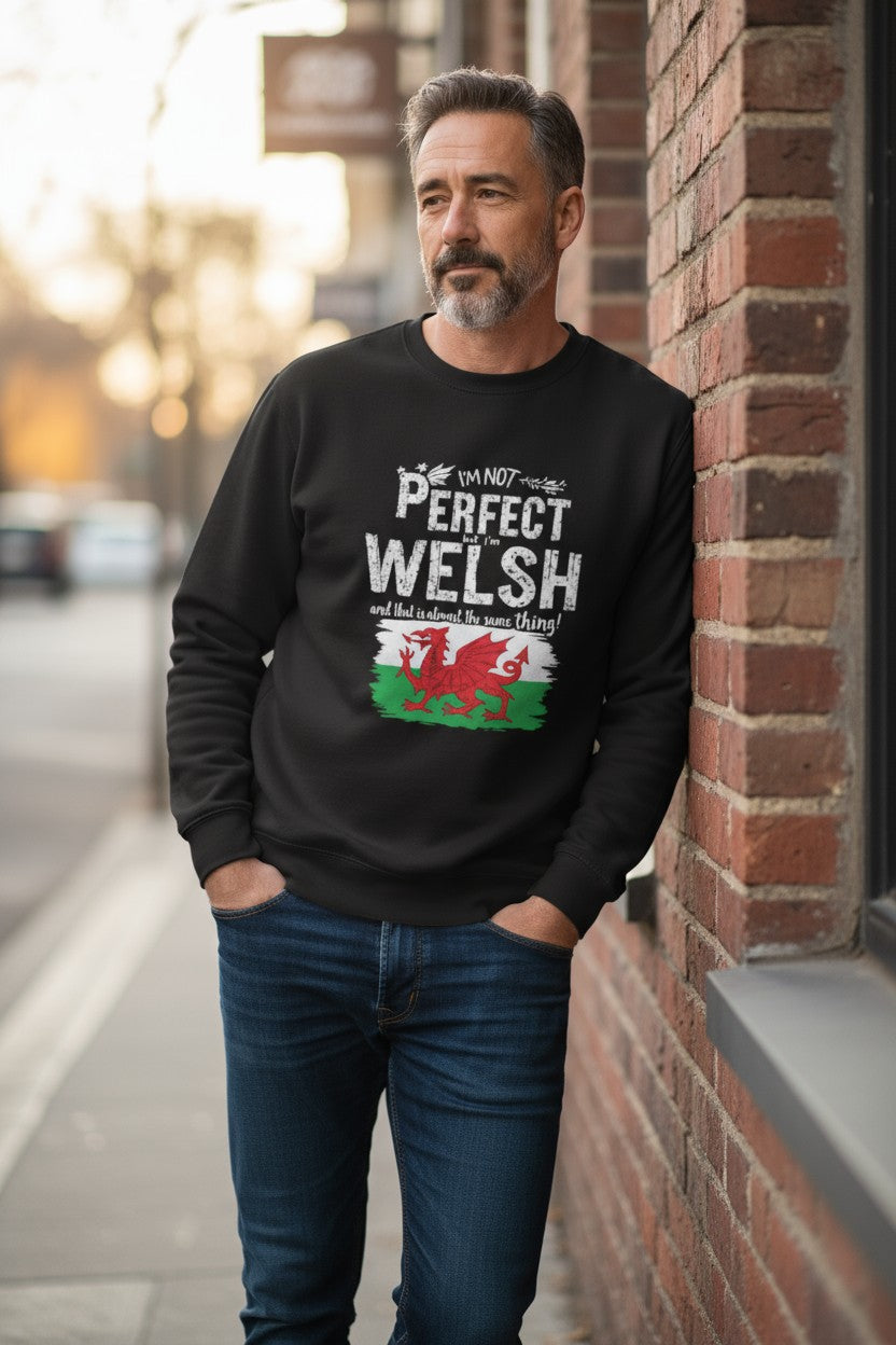 Man wearing a black sweatshirt with Welsh text and flag design, standing against a brick wall.