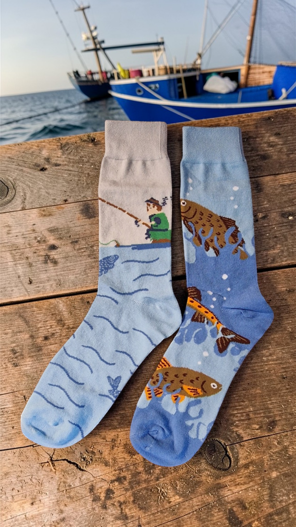 Two socks with fishing design on a wooden surface near water and a boat.