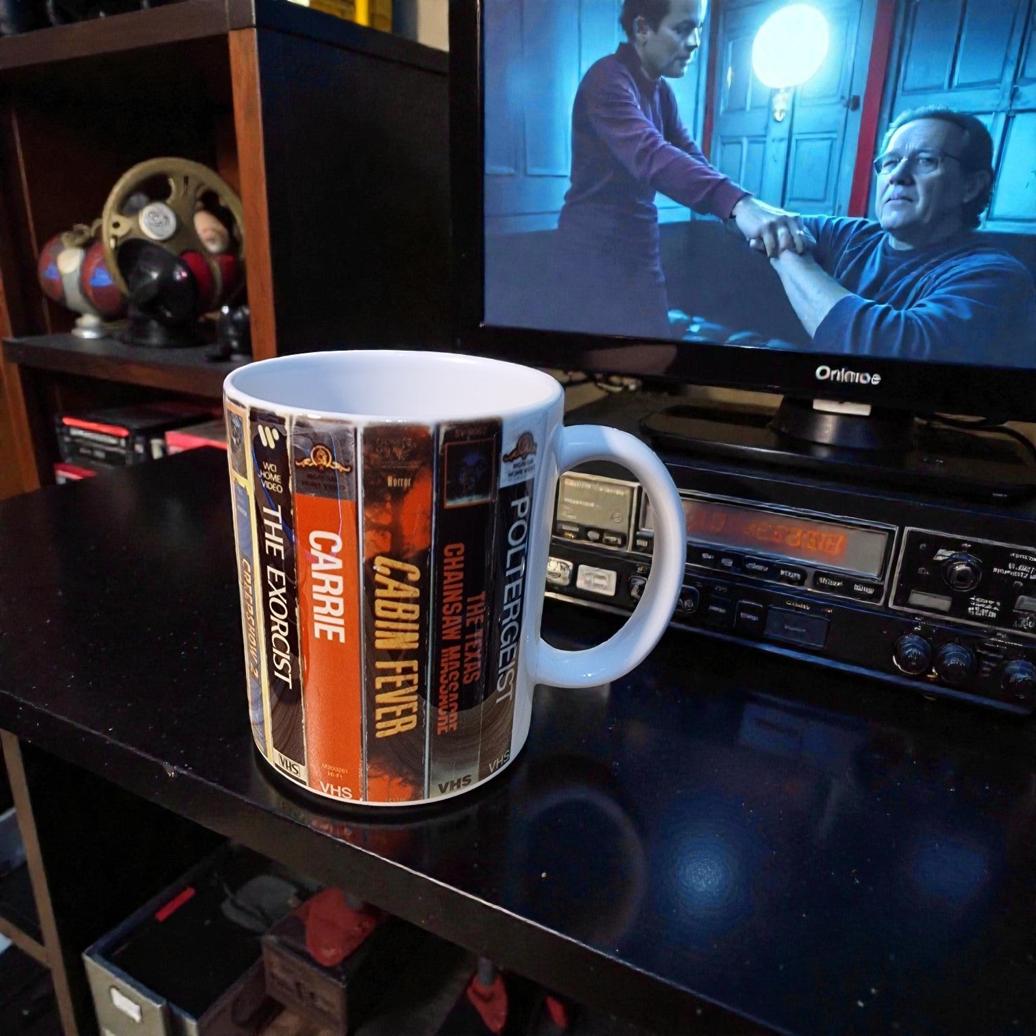 Mug with book cover design on a table in front of a television showing two men shaking hands.