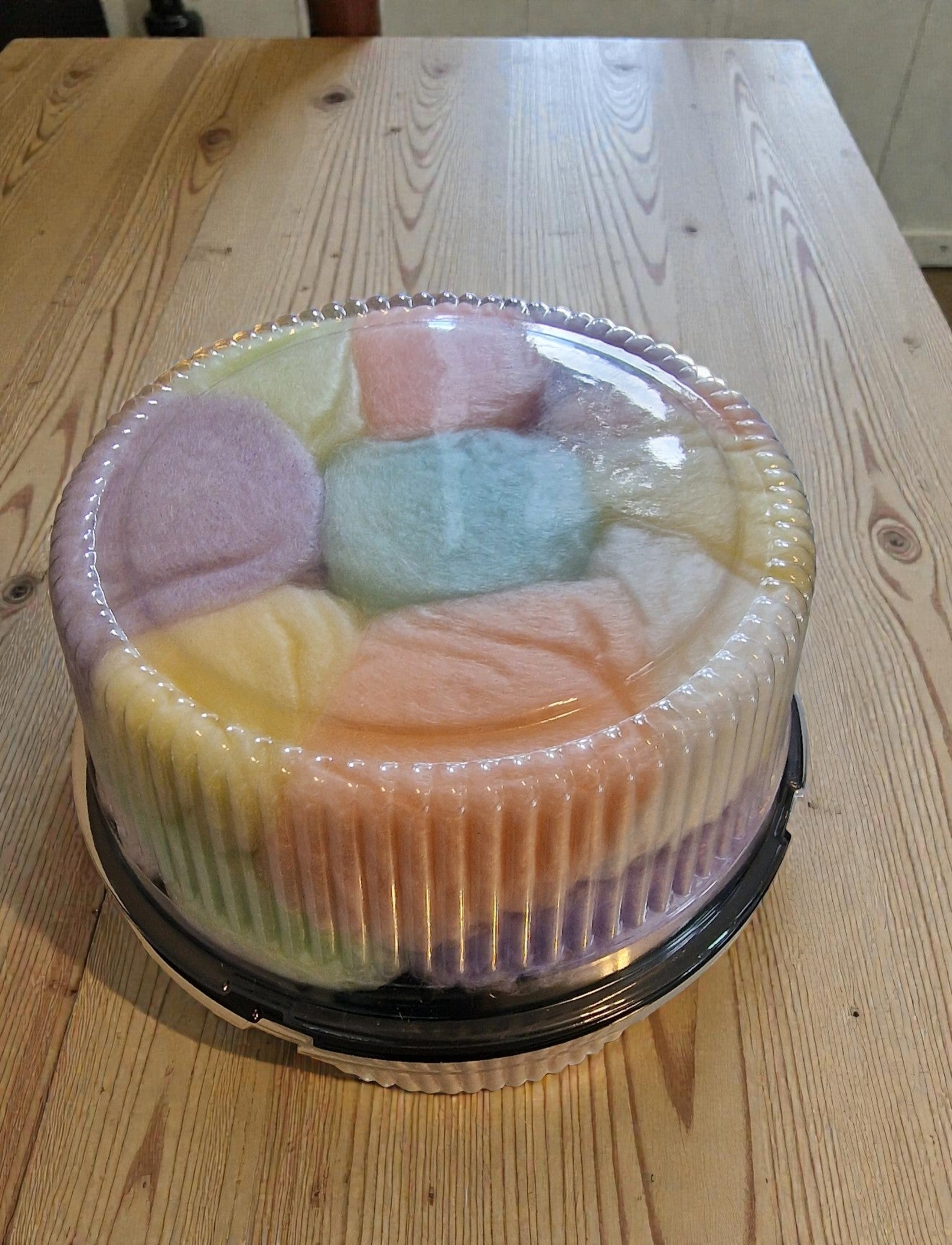 Pastel-colored cake with a clear plastic cover on a wooden table